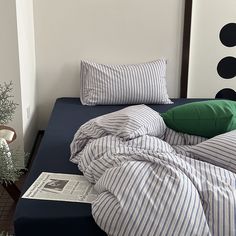 an unmade bed with blue and white sheets on it, next to a potted plant