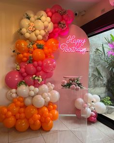 balloons and flowers on display in front of a pink wall with the words happy birthday