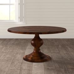 a round wooden table sitting on top of a hard wood floor next to a window