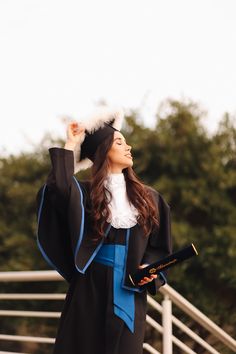 a woman wearing a graduation gown and holding her hat in the air with one hand