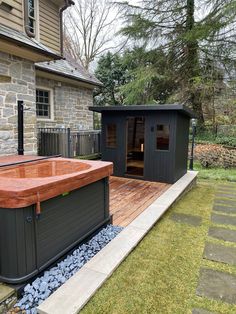 a hot tub sitting on top of a wooden deck next to a stone building and grass