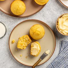 two muffins on plates with butter and some other dessert items next to them