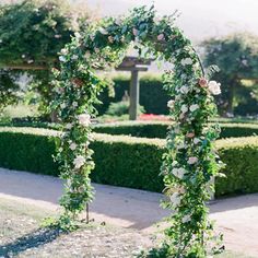 an arch covered with flowers and greenery in the middle of a garden