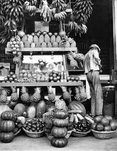 an old black and white photo of fruit stand with bananas, pineapples, melons, etc