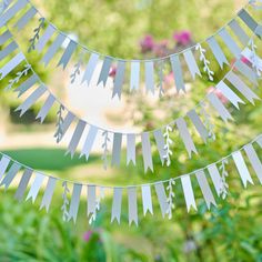 some white paper cutouts are hanging from a string in front of green grass and flowers