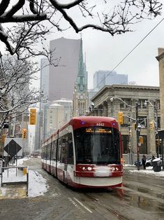 a red and white train traveling down tracks next to tall buildings on a snowy day