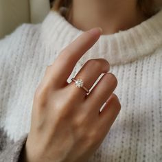 a woman's hand with a diamond ring on her finger, wearing a white sweater