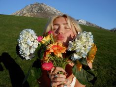 a woman holding flowers in front of her face and making a funny face while sitting on the grass