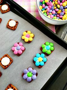 there are many small flowers on the cookie sheet next to a bowl of candies