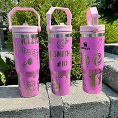 two pink tumblers sitting next to each other on top of a stone wall with plants in the background