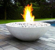 a fire pit sitting on top of a brick patio next to a swimming pool with trees in the background