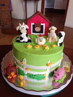 a green cake with farm animals on it and a red barn in the back ground