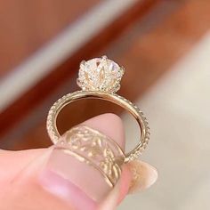 a close up of a person's hand holding a ring with a diamond on it