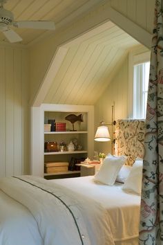 a white bed sitting under a window next to a wall mounted ceiling fan in a bedroom