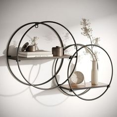 two circular metal shelves with books and vases on them against a white wall,