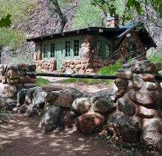 there is a rock wall with a house in the back ground and trees around it