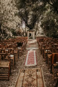 an outdoor wedding venue with rows of wooden chairs and rugs on the ground, surrounded by trees