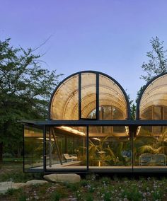 two large glass buildings sitting on top of a lush green field next to trees and bushes