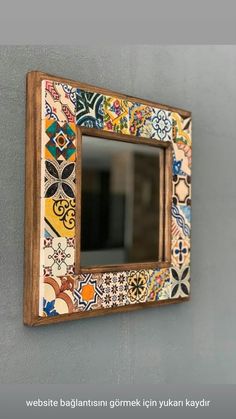 a mirror mounted to the side of a wall with colorful tiles on it's sides