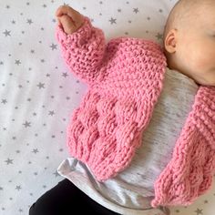 a baby wearing a pink knitted sweater laying on top of a white bed with stars