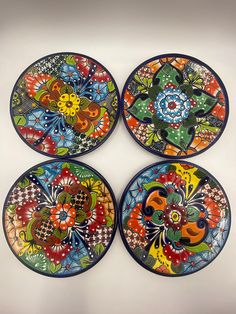 four colorful plates with designs on them sitting on a table