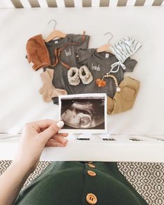 a person holding up a baby's photo in front of a wall with clothes on it