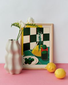 two lemons sit next to a vase with flowers in it on a pink surface