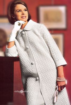 a woman in a white coat and dress is posing for a photo with her hand on her chin