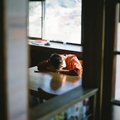 a young boy sleeping on top of a wooden table in front of a large window