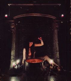 a woman sitting on the floor in front of a barrel with candles around her legs