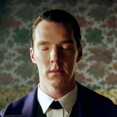 a man wearing a suit and tie in front of a floral wallpapered background