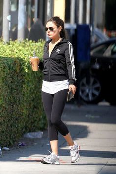 a woman in black jacket and leggings walking down the street with a drink