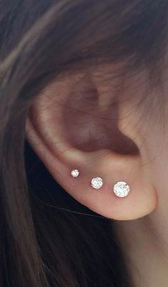 a close up of a person wearing three different piercings on their ears and behind them is a woman's ear