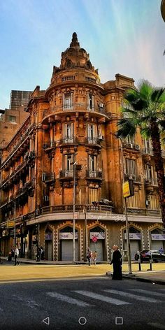 an old building in the middle of a street with palm trees and people walking around