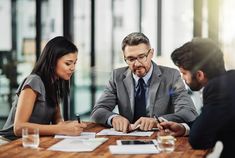 three business people sitting at a table discussing paperwork