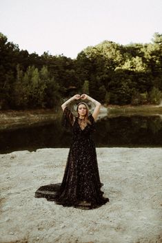 a woman in a black dress is standing on the beach with her arms above her head