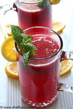 two glasses filled with red liquid and garnished with mint on the rims