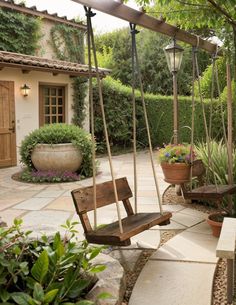 a wooden swing sitting in the middle of a garden next to a tree and potted plants