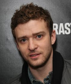 a man standing in front of a black backdrop wearing a leather jacket and scarf, looking at the camera