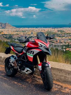 a red and black motorcycle parked on the side of a road next to a hill