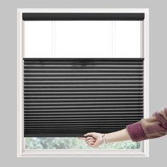 a woman standing in front of a window with the blinds pulled up to look out