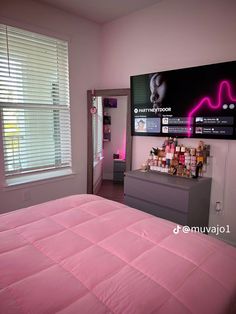 a bedroom with pink bedding and a large television mounted on the wall above it