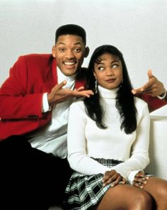 a man and woman sitting on top of a white couch posing for a photo with their hands in the air