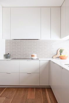 a kitchen with white cabinets and wood floors is pictured in this image, there are plants on the counter