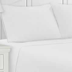 a bed with white sheets and pillows on top of it next to a night stand