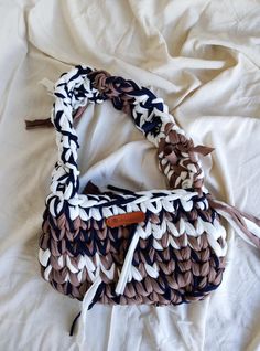 a woven purse sitting on top of a white bed covered in sheets and pillows,