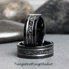 two wedding bands with black and white diamonds in them on top of each other next to some rocks