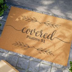 a door mat with the words covered in leaves on it and a box next to it