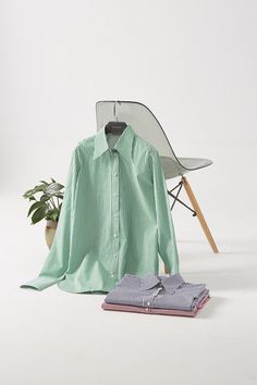 a green shirt sitting on top of a white chair next to a potted plant