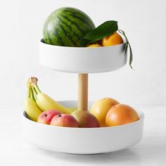 two tiered bowls with fruit in them and one on top of the bowl holding bananas, oranges, apples, and watermelon